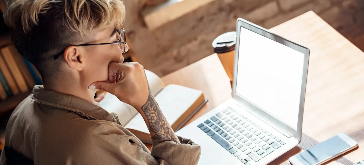 [Featured image] A learner wearing glasses studies how to stop procrastinating with an open book and a silver laptop computer.