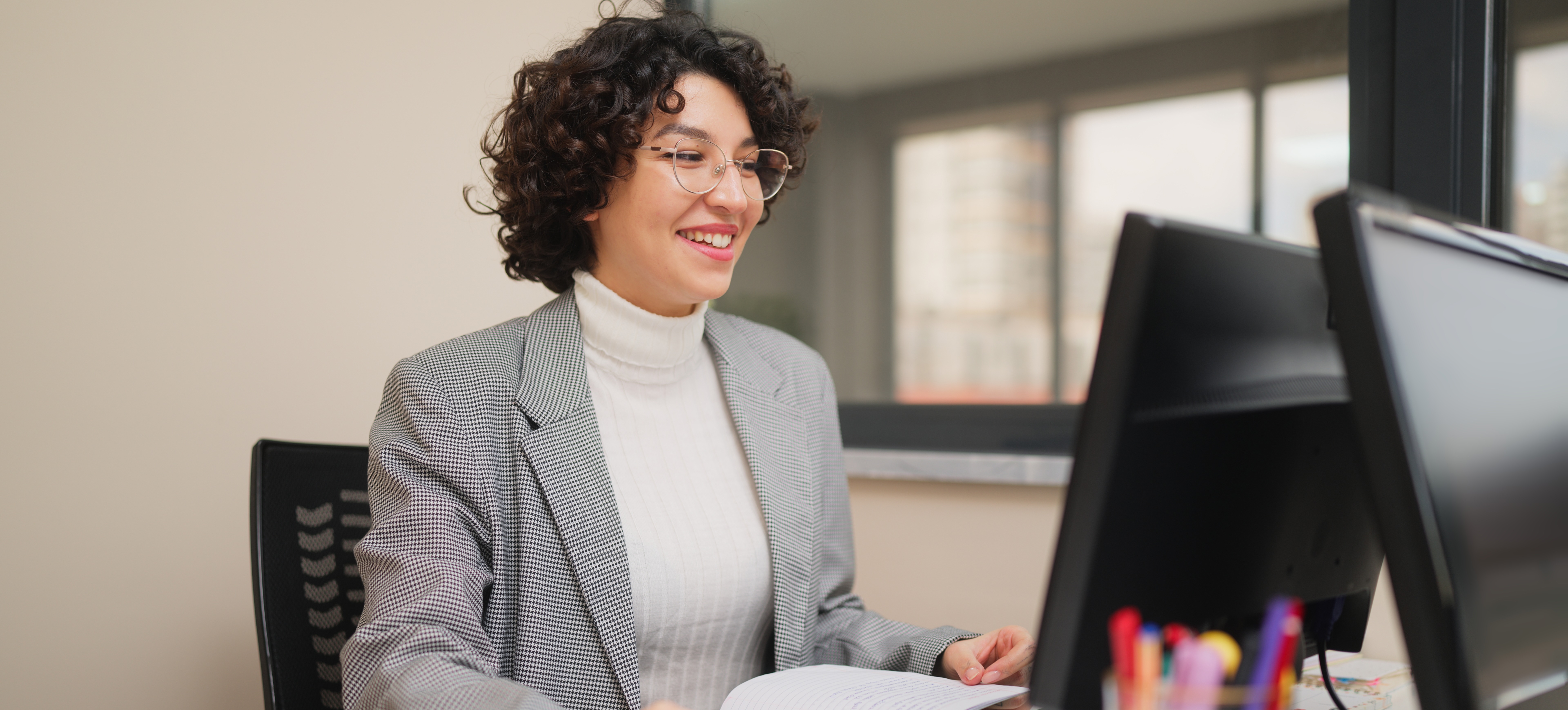 [Featured Image] A smiling content creator working for a marketing firm uses their content optimization skills as they work at their computer.
