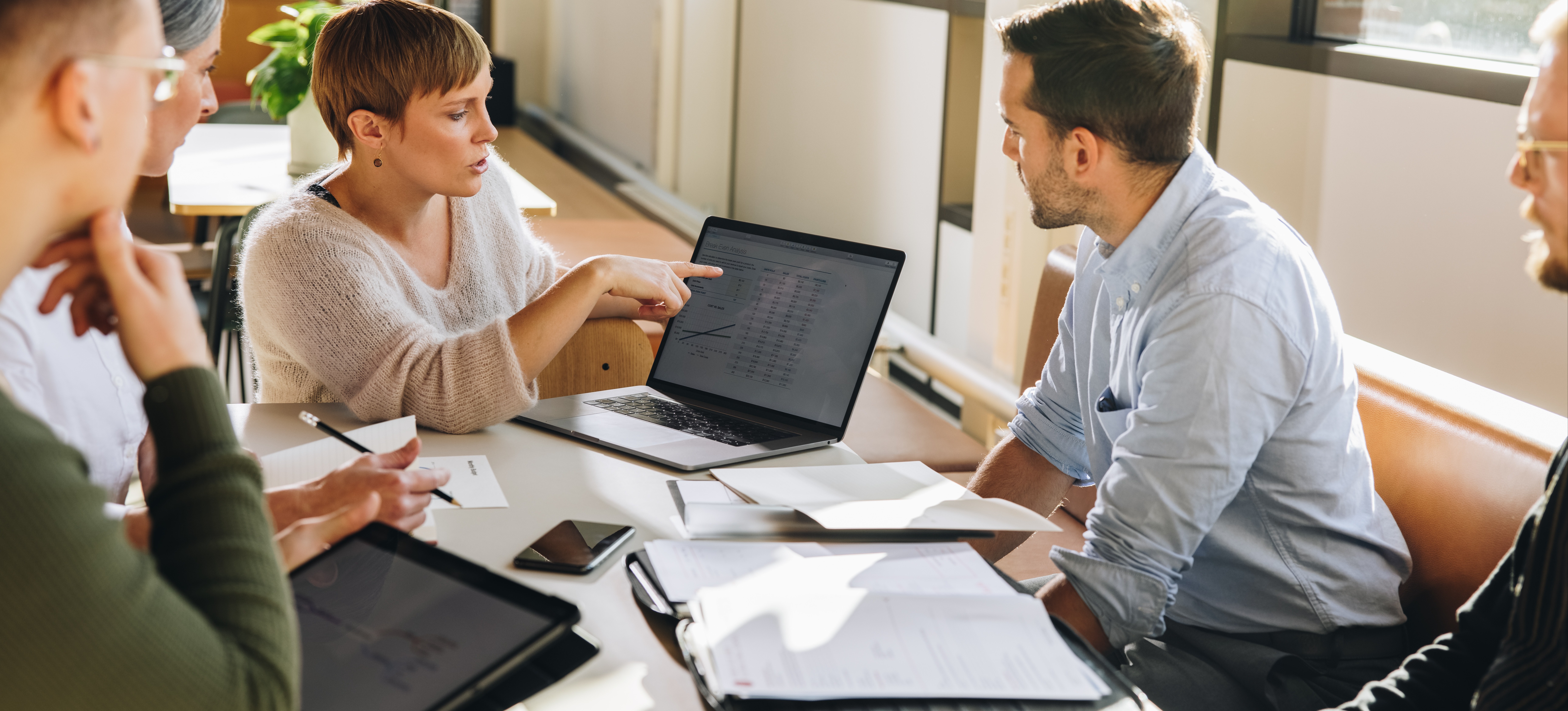 [Featured Image] In a meeting, a business person answers the question, what is defi, as they talk to their colleagues and shows them data on their laptop screen.
