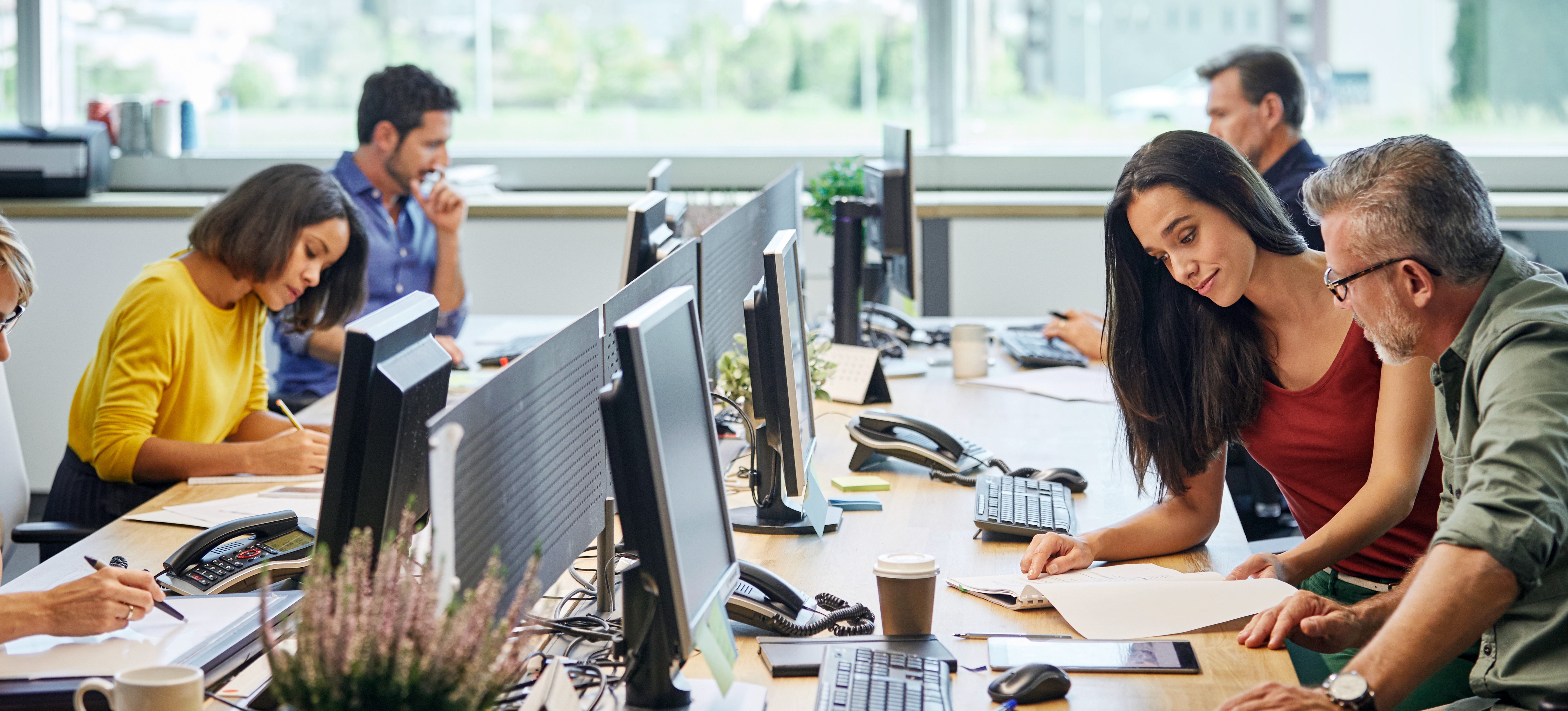 [Featured Image] After learning what is bandwidth and the benefits of high bandwidth, a group of businesspeople work on their computers simultaneously, talking amongst themselves and collaborating.
