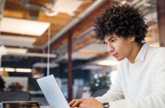 [Featured image] A person in a white sweater sits at a table in a co-working space and works on computer graphics on their laptop.