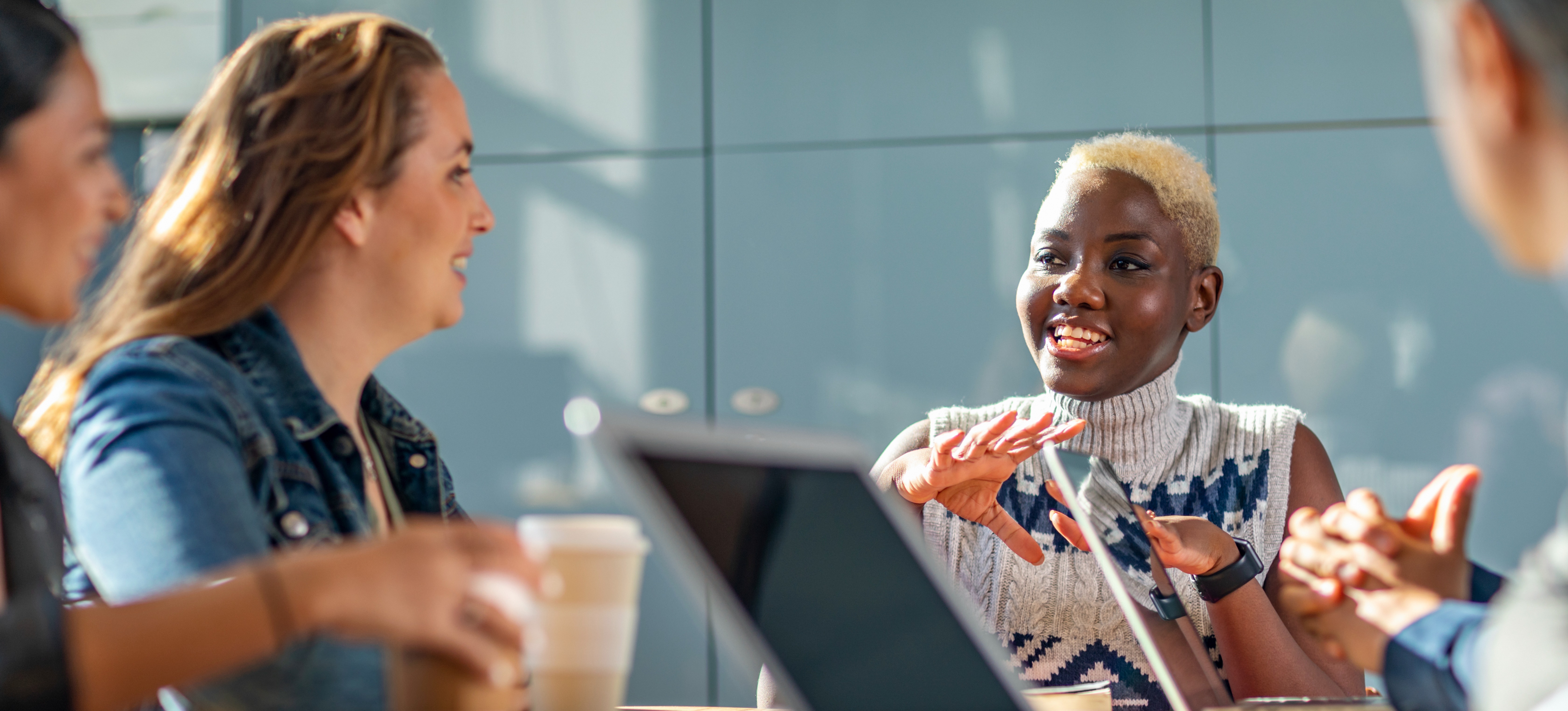 [Image en vedette] Eine Frau in einer Besprechung nutzt einen beispielhaften Elevator Pitch, um ihr Projekt schnell den drei anderen Geschäftsmännern vorzustellen, die um sie herum am Tisch sitzen.