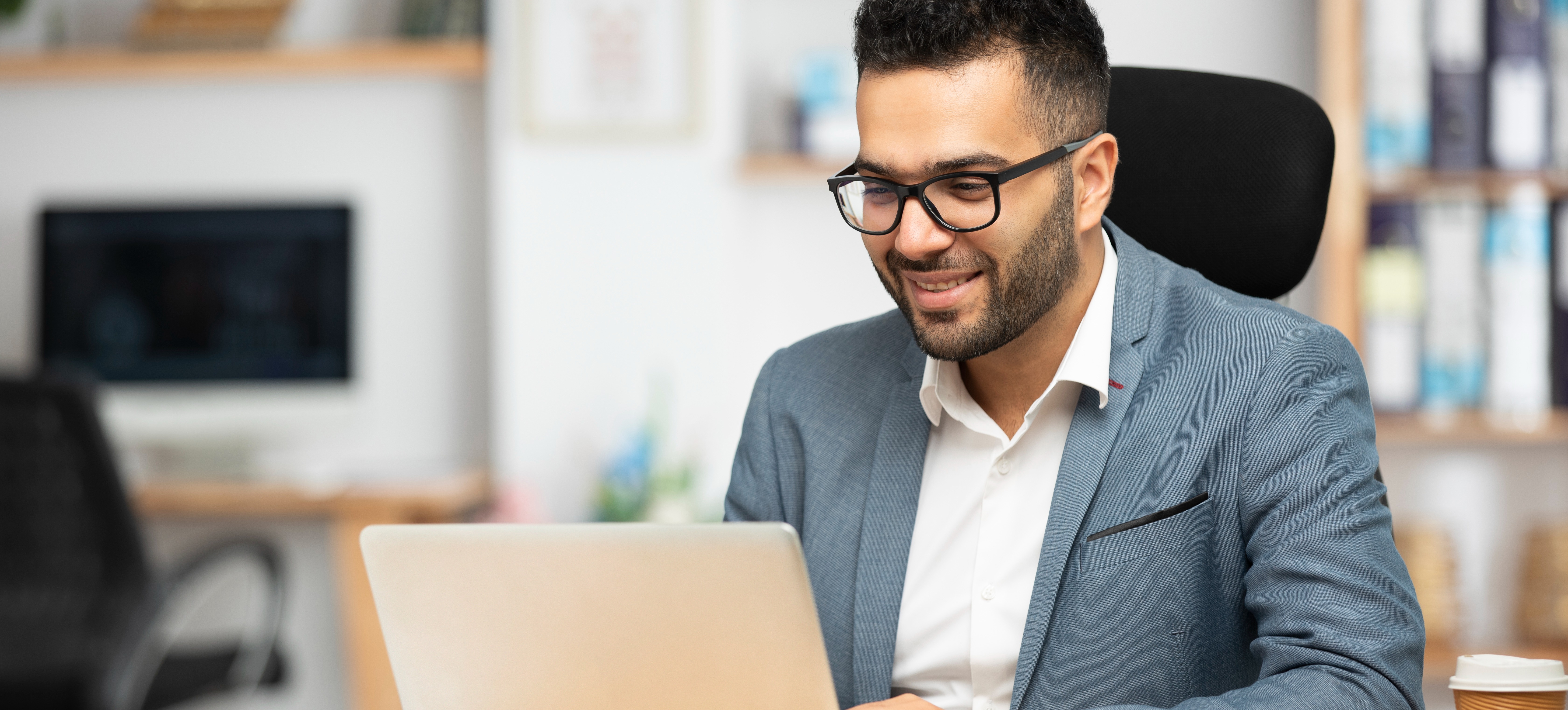 [Featured Image] A smiling blockchain developer types on their laptop in an office.
