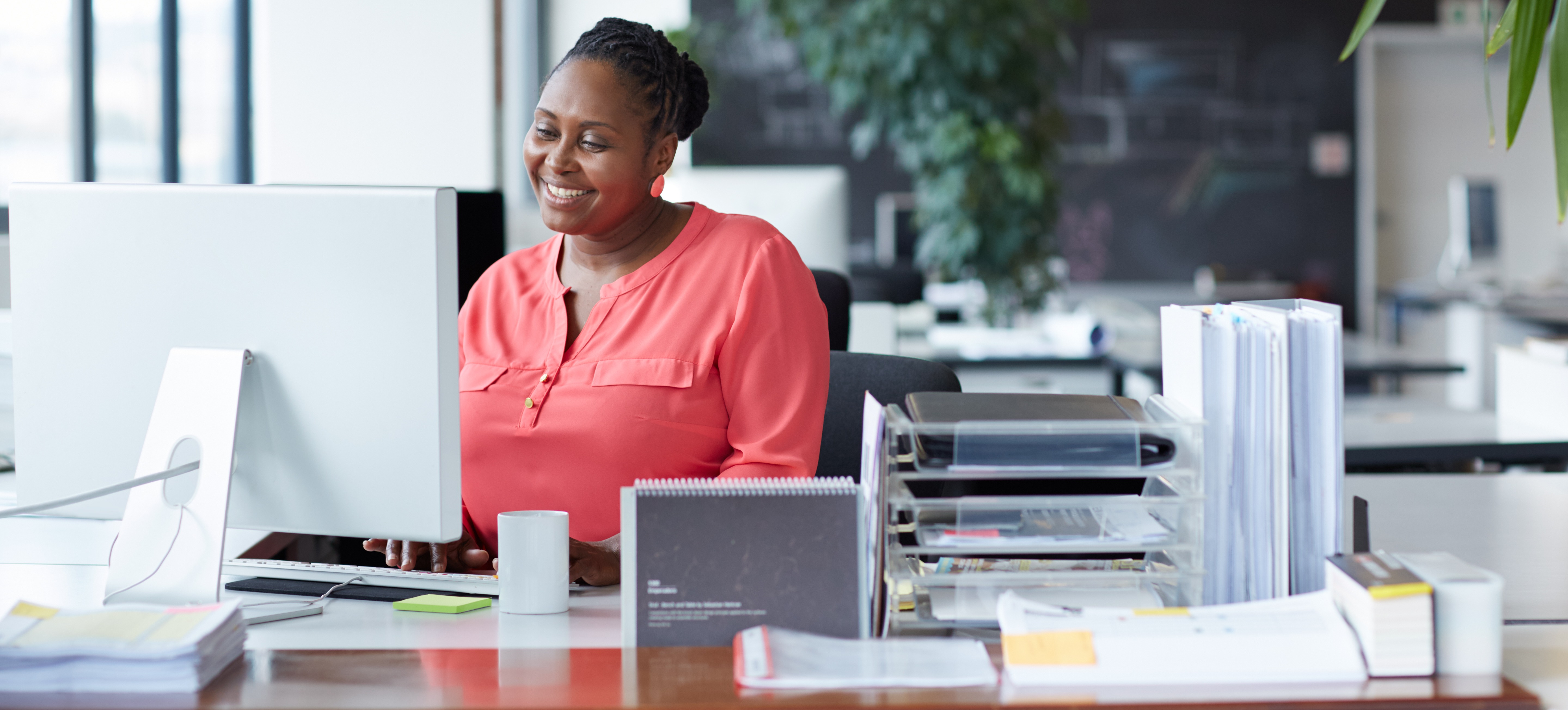 [Featured Image] A smiling person works at their desktop computer in an office.