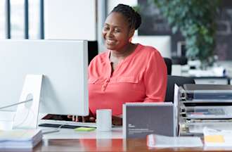 [Featured Image] A woman works at a desktop computer in an office.