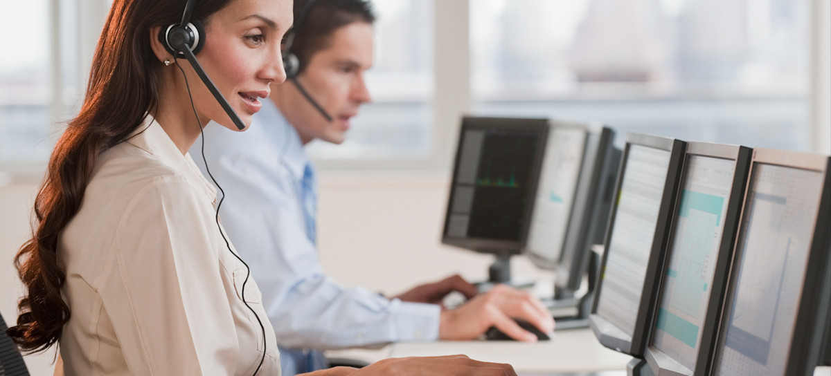 [Featured Image] An IT specialist wears a headset and works on a computer while helping a customer understand what a mesh network is. 