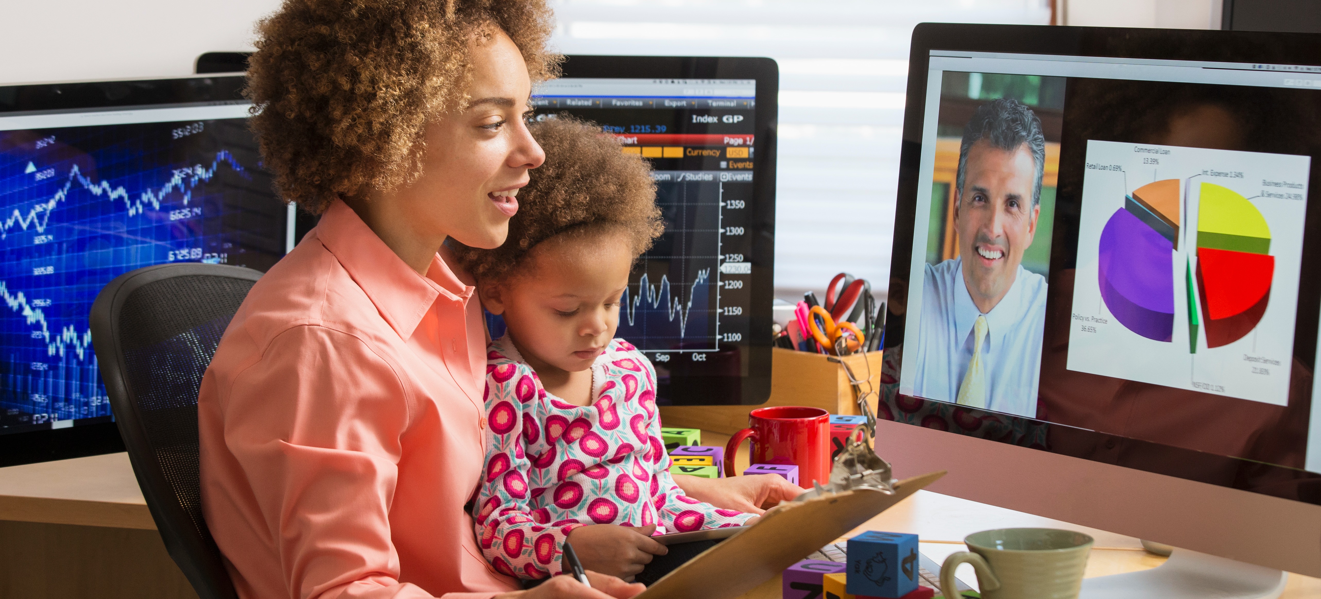 [Featured Image] A professional working in their home office with their toddler on their lap has a video conference with a colleague while looking at an exploding pie chart on their computer monitor.
