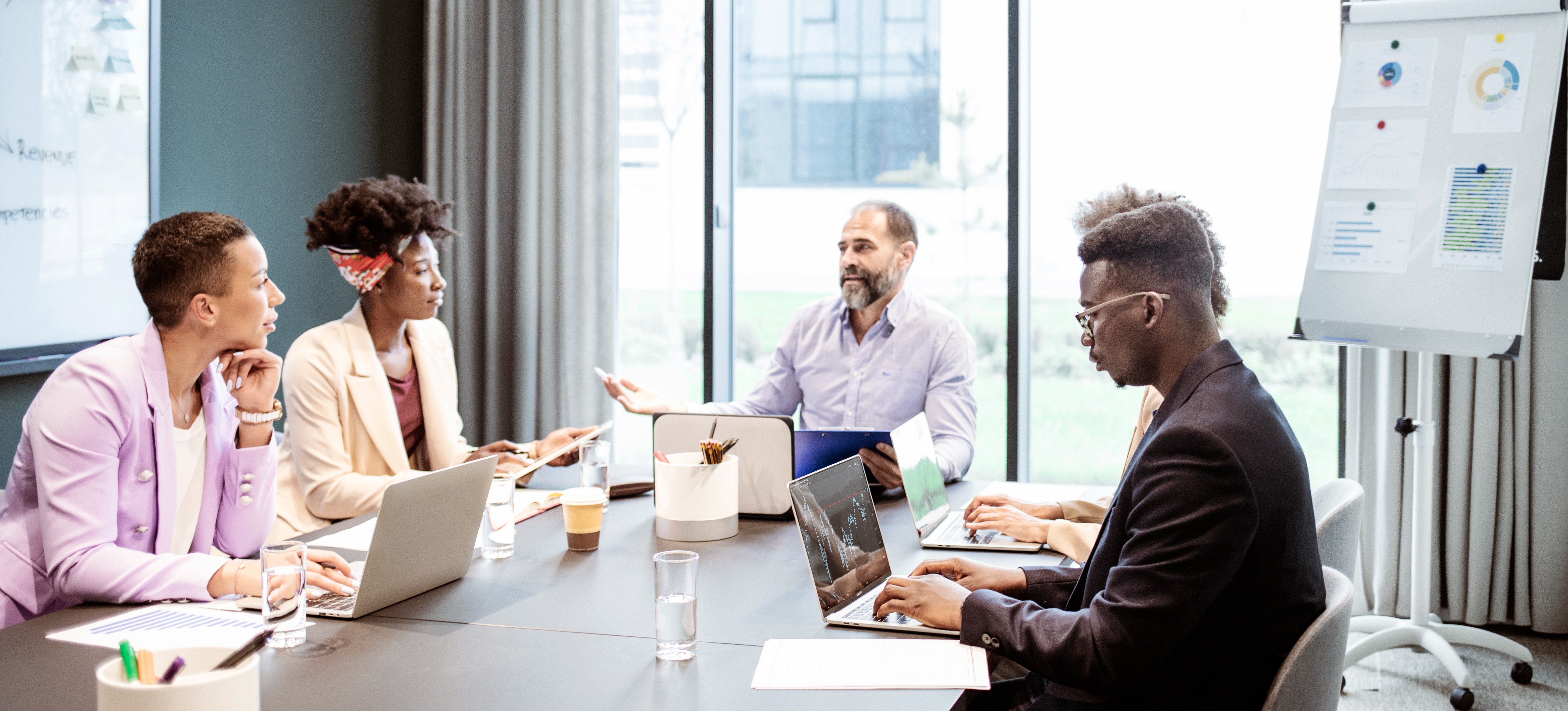 [Image en vedette] Des professionnels se réunissent autour d'une table dans une salle de conférence bien éclairée, chacun sur un ordinateur portable connecté via un point d'accès sans fil, discutant des statistiques et des projets commerciaux.