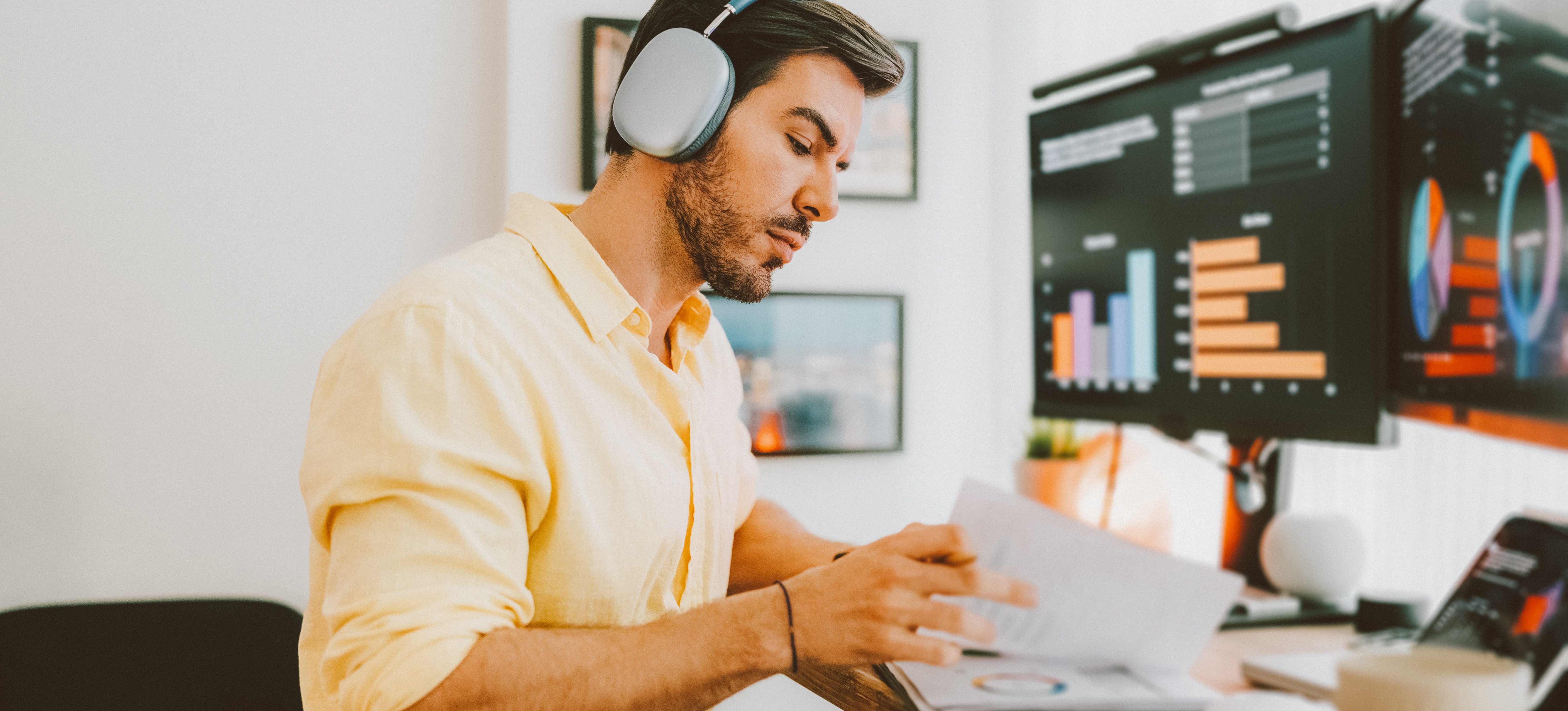 [Featured Image] A professional working with dynamic named ranges at a standing desk, using headphones while analyzing graphs on his computer in a professional workspace.
