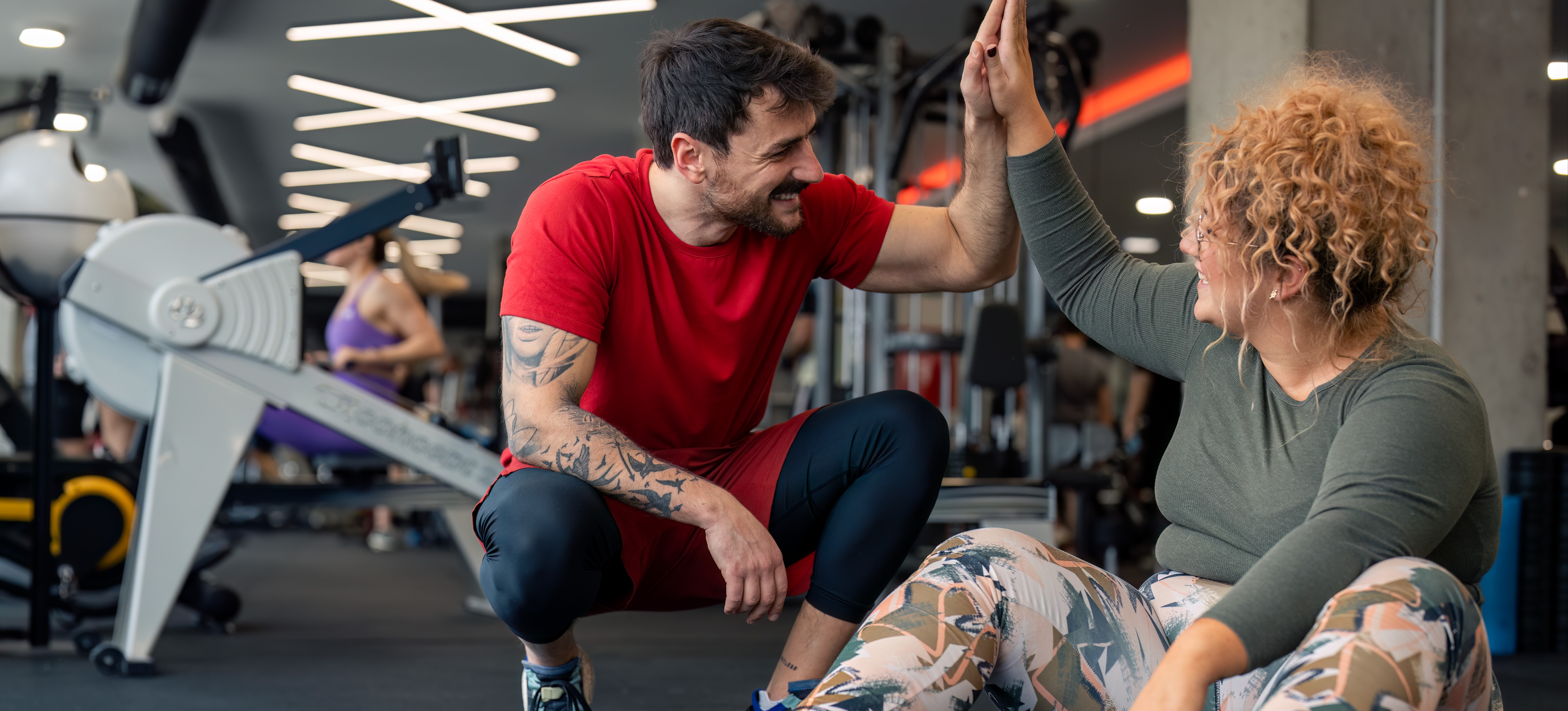 [Featured Image] A personal trainer gives a high-five to a client as they complete a set of weight lifting in a gym.
