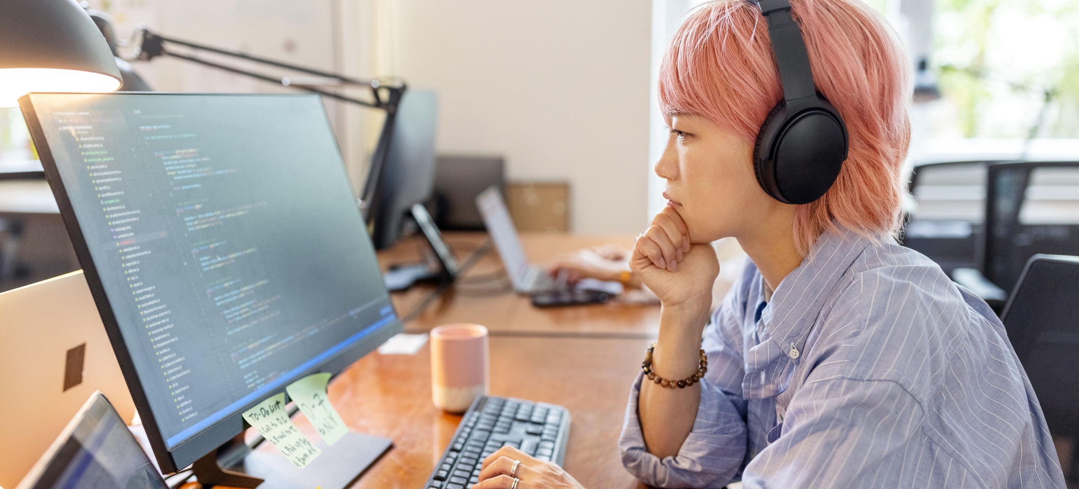 [Featured Image]: A computer programmer wearing headphones looks at a computer monitor as they consider algorithmic design in their work.
