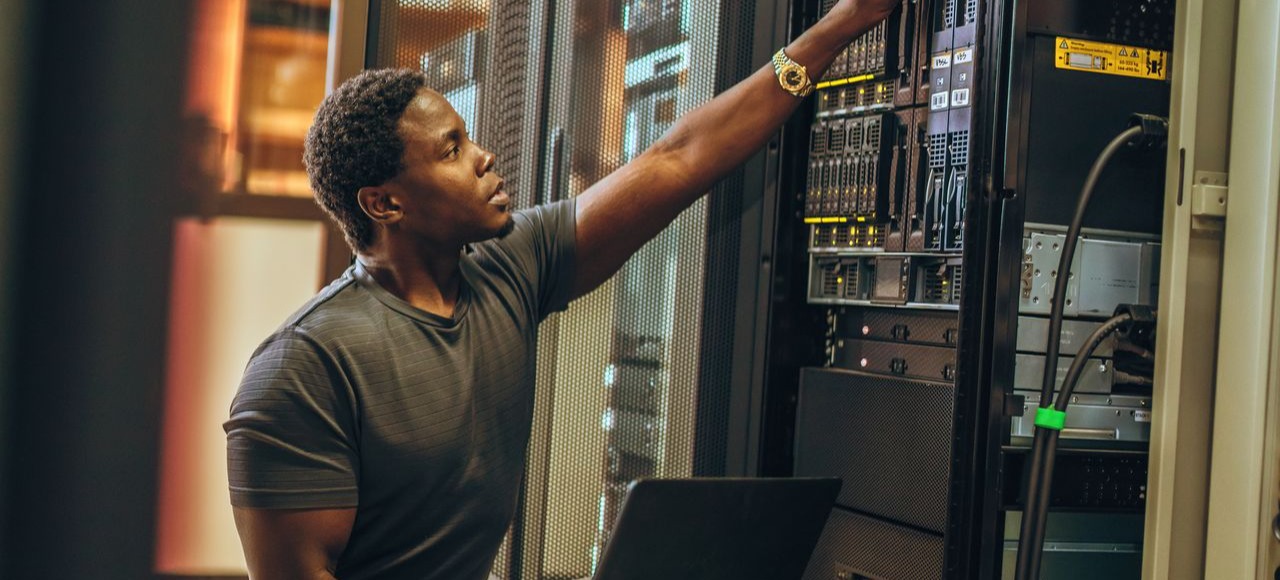 [Featured image] A cybersecurity analyst is working with physical servers while holding a laptop.