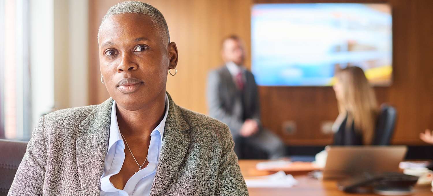 [Image] A woman in a blazer and button-down shirt sits at a conference table.