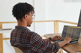 [Featured image] An ethical hacker in a plaid shirt and glasses competes to win a bug bounty on a laptop computer while sitting at a desk with a large desktop monitor.