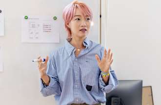 [Featured image] A UX project manager stands in front of a whiteboard and gives a presentation to their team. 
