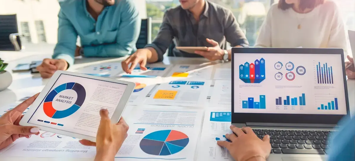 [Featured Image] A group of data analysts engaged in a discussion in a professional setting, reviewing graphs and charts displayed on both paper and a computer screen while comparing R and Tableau for data analysis and visualization.
