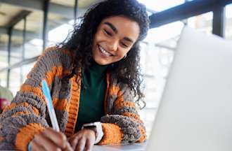 A college student is seen writing notes and working on a laptop.