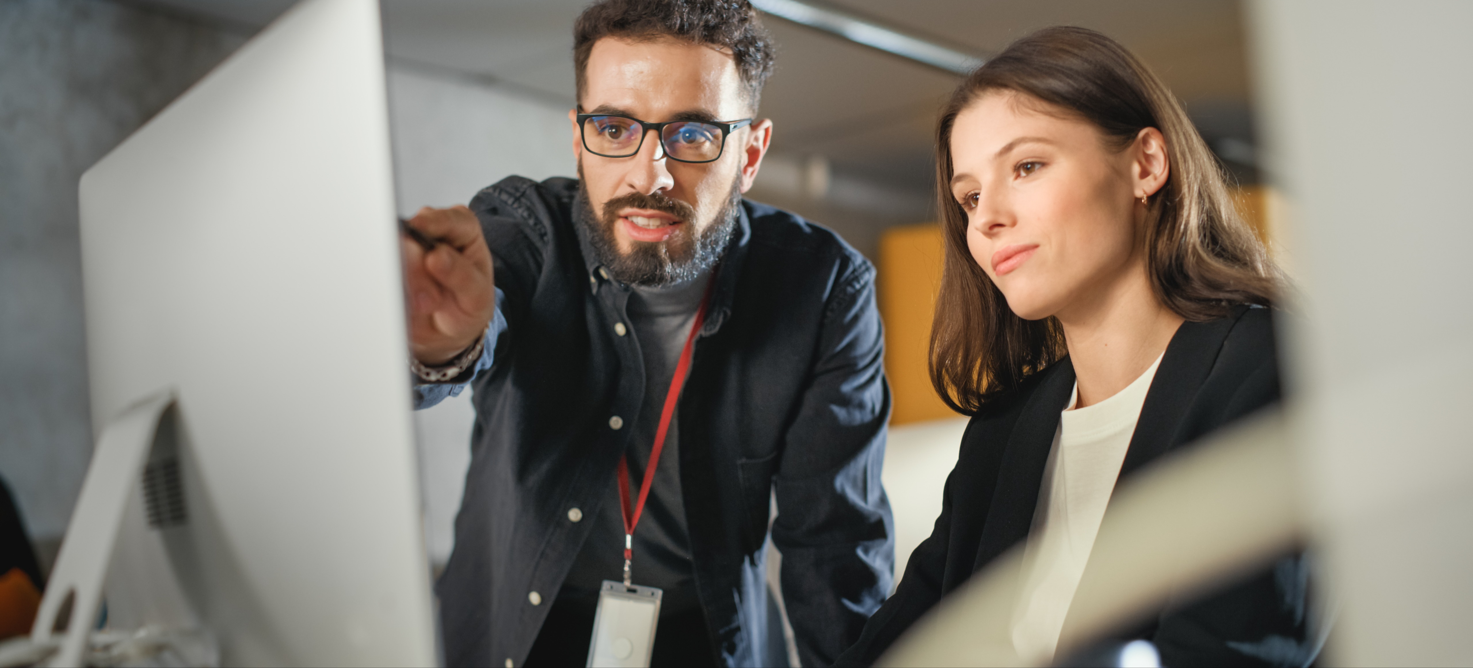 [Featured Image] A technical support analyst points at a computer screen to troubleshoot software issues with their colleague as they look on.