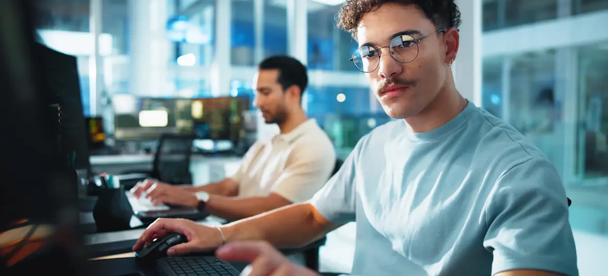 [Featured image] A programmer uses a Git commands cheat sheet as they work at a computer in a spacious office next to a coworker.

