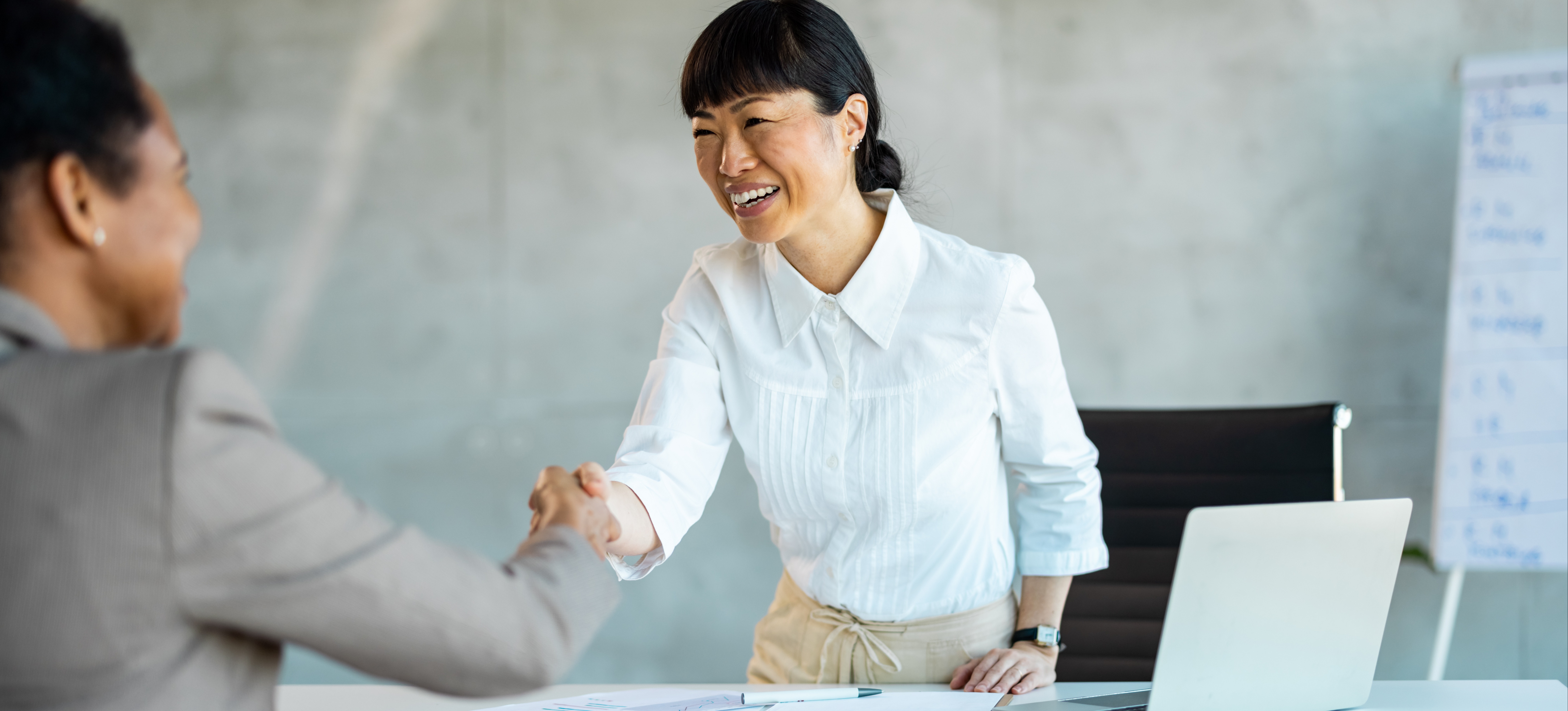 [Featured Image] A smiling employee stands and shakes the hand of their supervisor as they finish an exit interview.