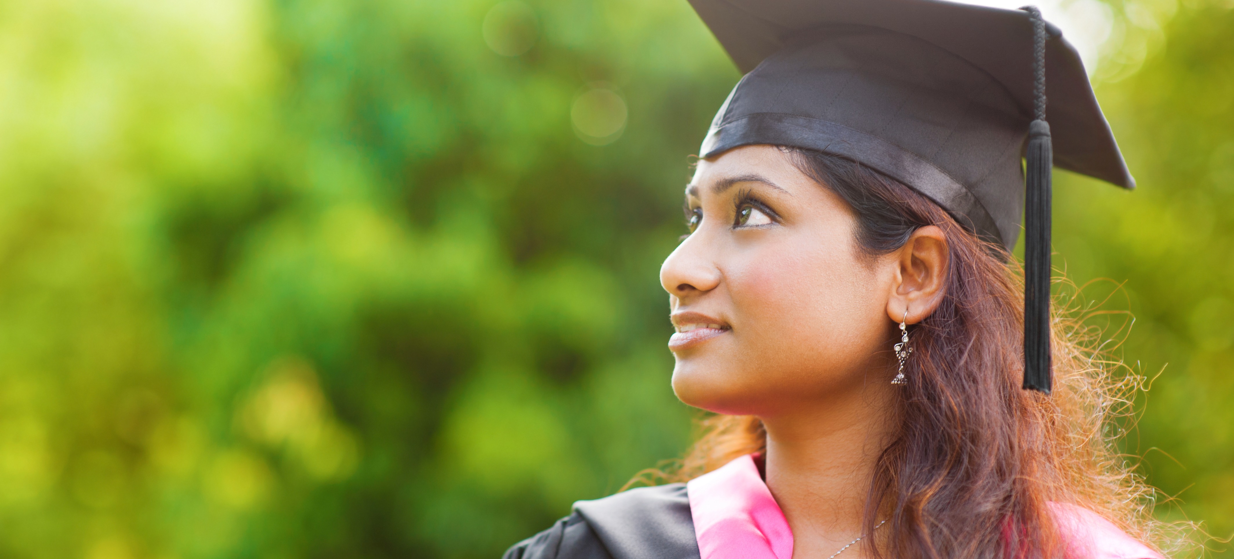 [Featured Image] Indian graduate in a black cap and gown thinking about whether an online MBA is valid in India. 
