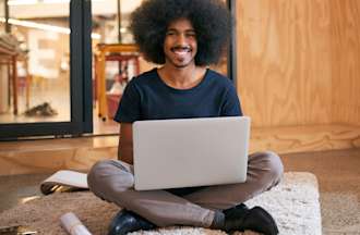 [Featured image] A front-end developer sits on a floor mat working on his laptop to build a website.