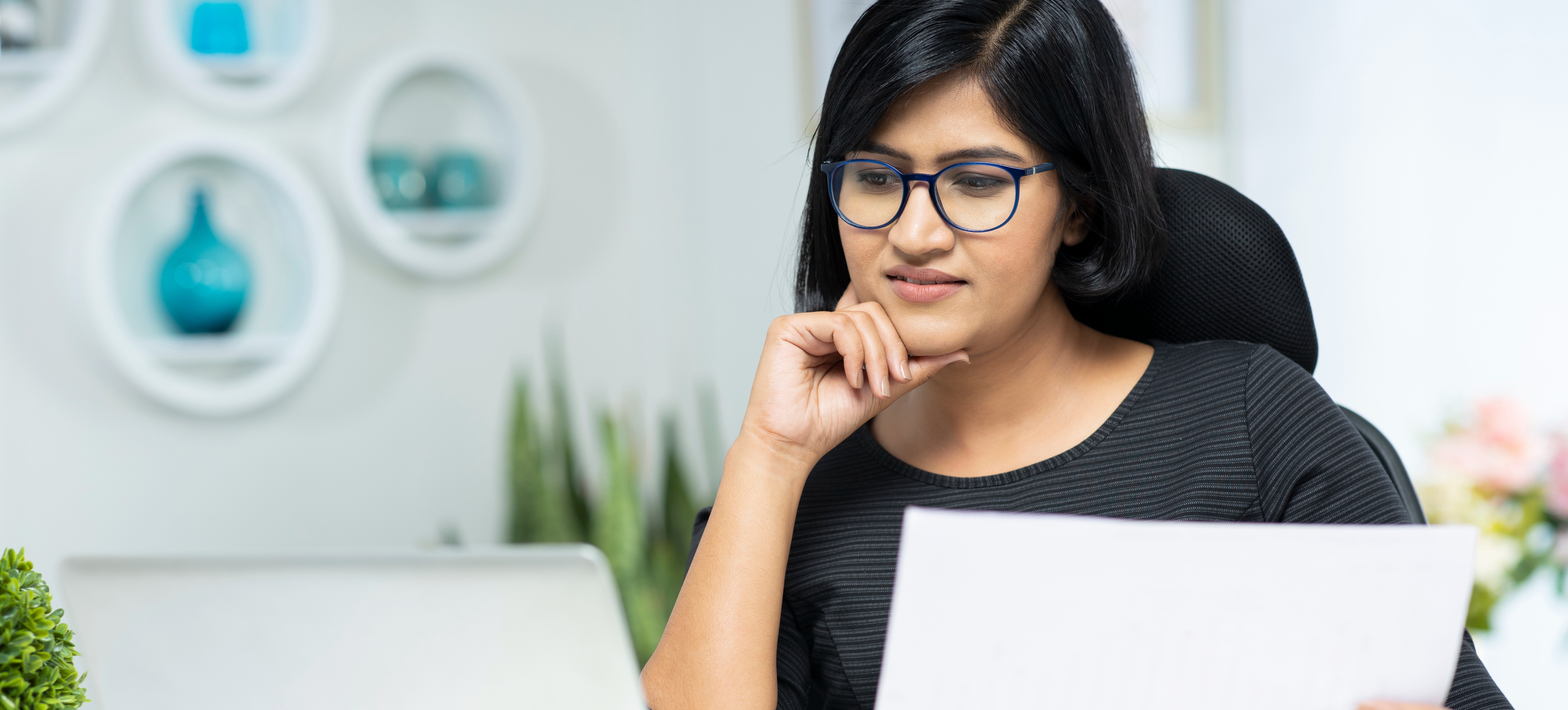 [Featured Image] A woman looks at the UPSC Optional Subject List on a laptop while holding a sheet of paper.

