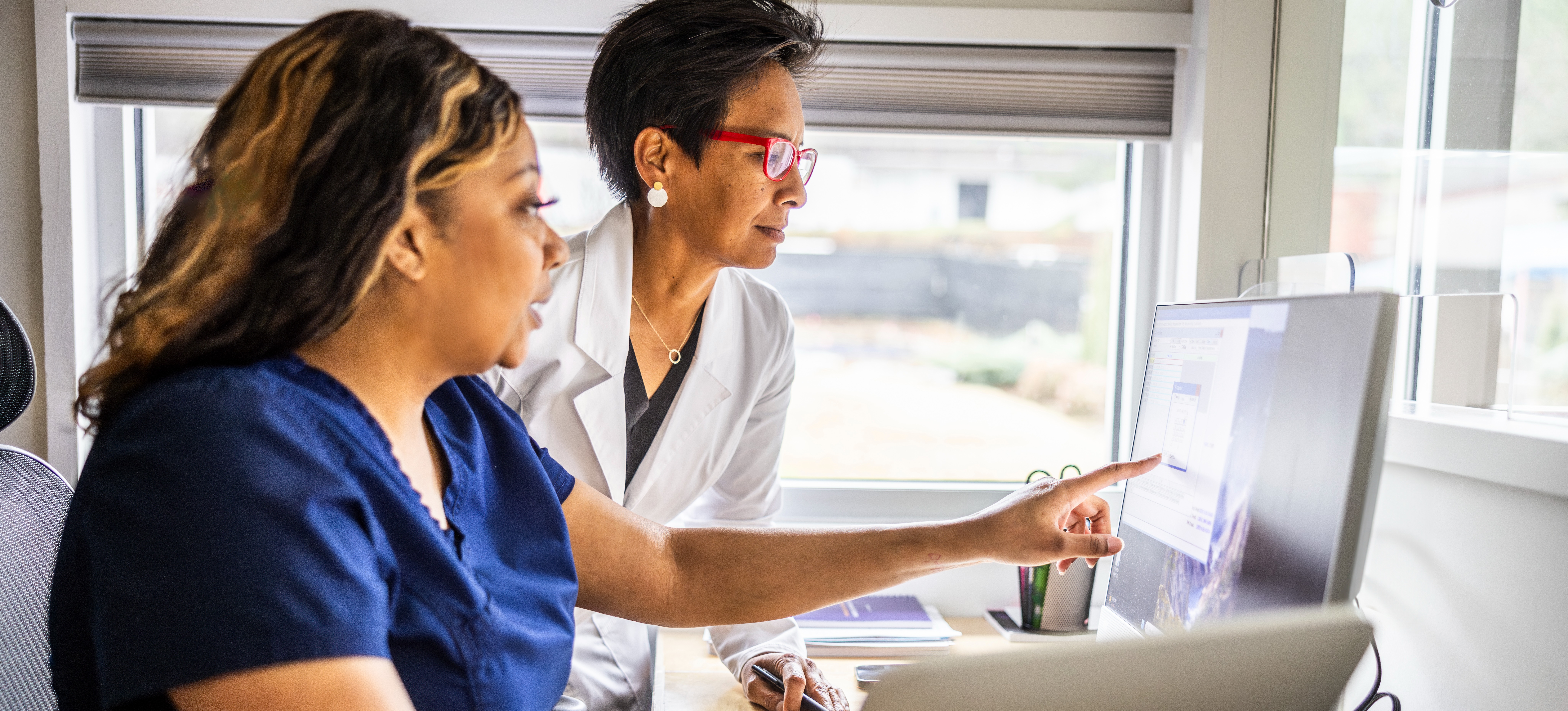 [Feature Image] After researching “How long does it take to become a registered nurse” on a desktop computer, an aspiring RN consults with an instructor to start planning their education.

