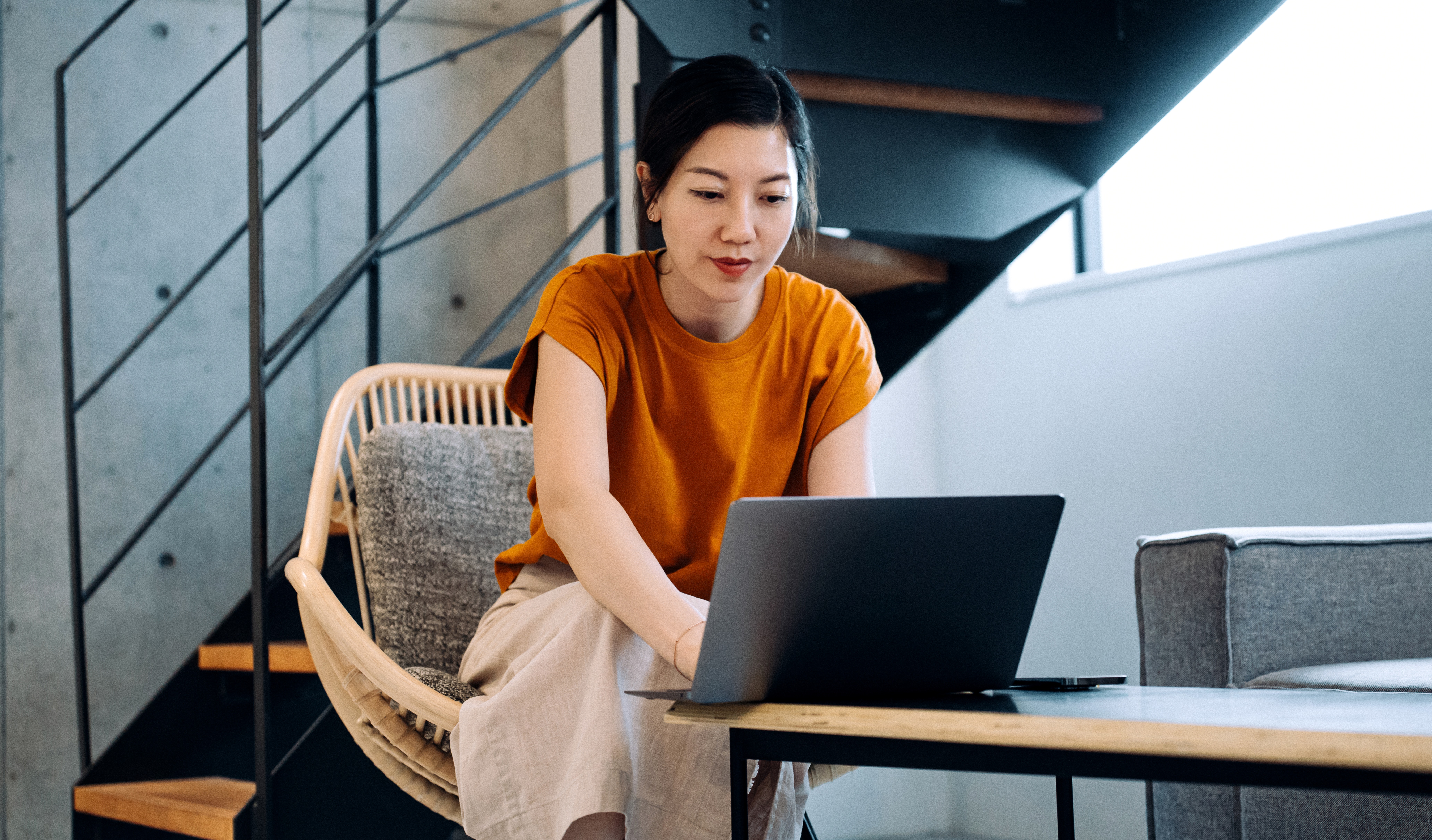 [Featured image] A cybersecurity analyst in a burnt orange shirt works on a laptop computer in a modern office setting.