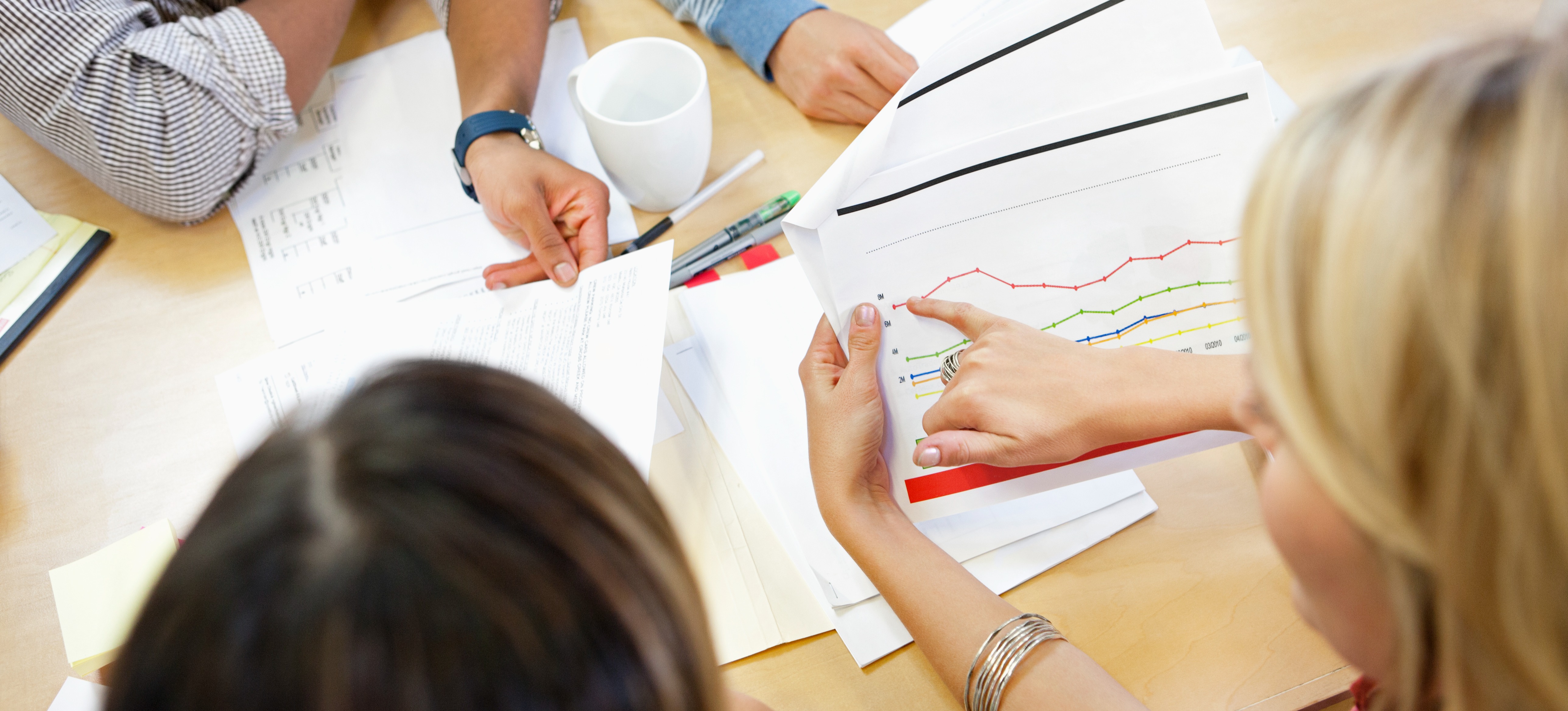 [Featured Image] A business team are in a meeting looking at graphs that show the tracking of their kpi's.