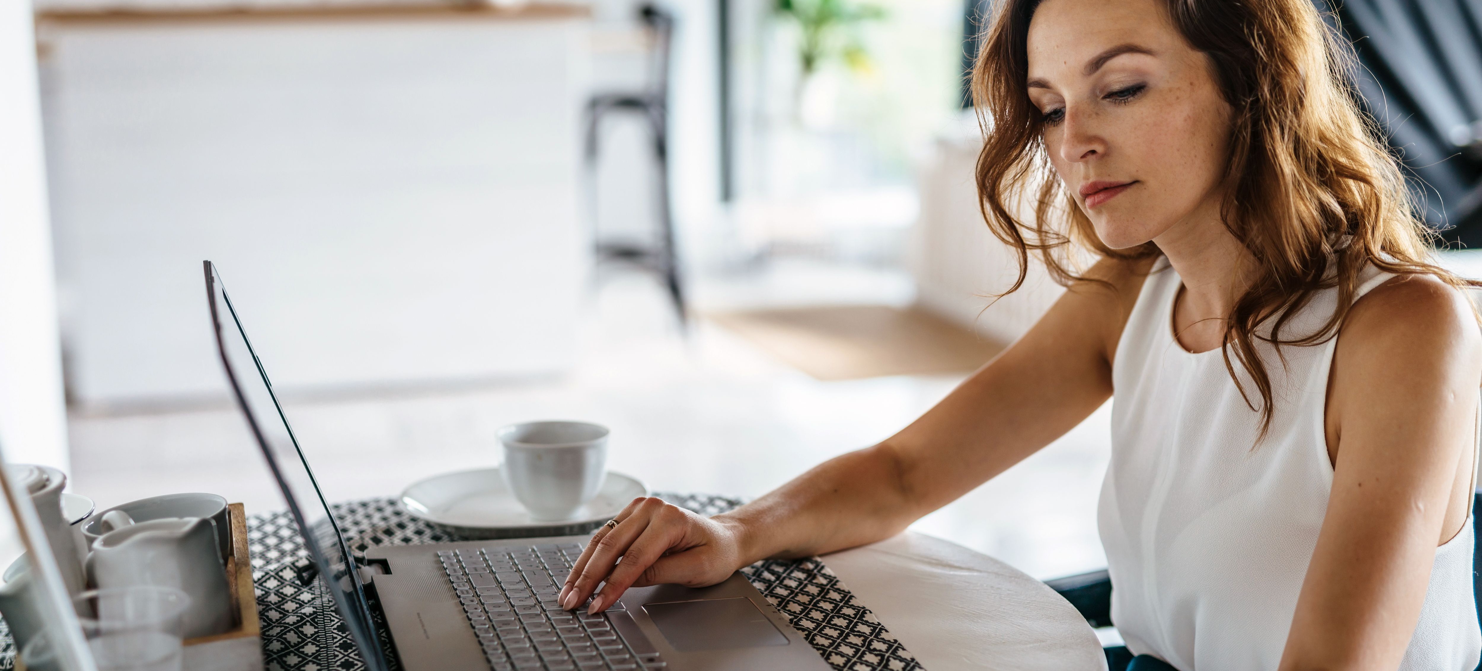 [Featured Image] A person is working on their laptop while holding papers.  