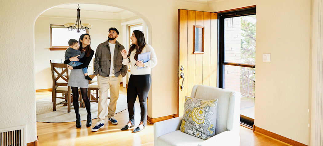 [Featured Image] A real estate agent practices their real estate agent skills as they give a house tour to a young family who are potential buyers.
