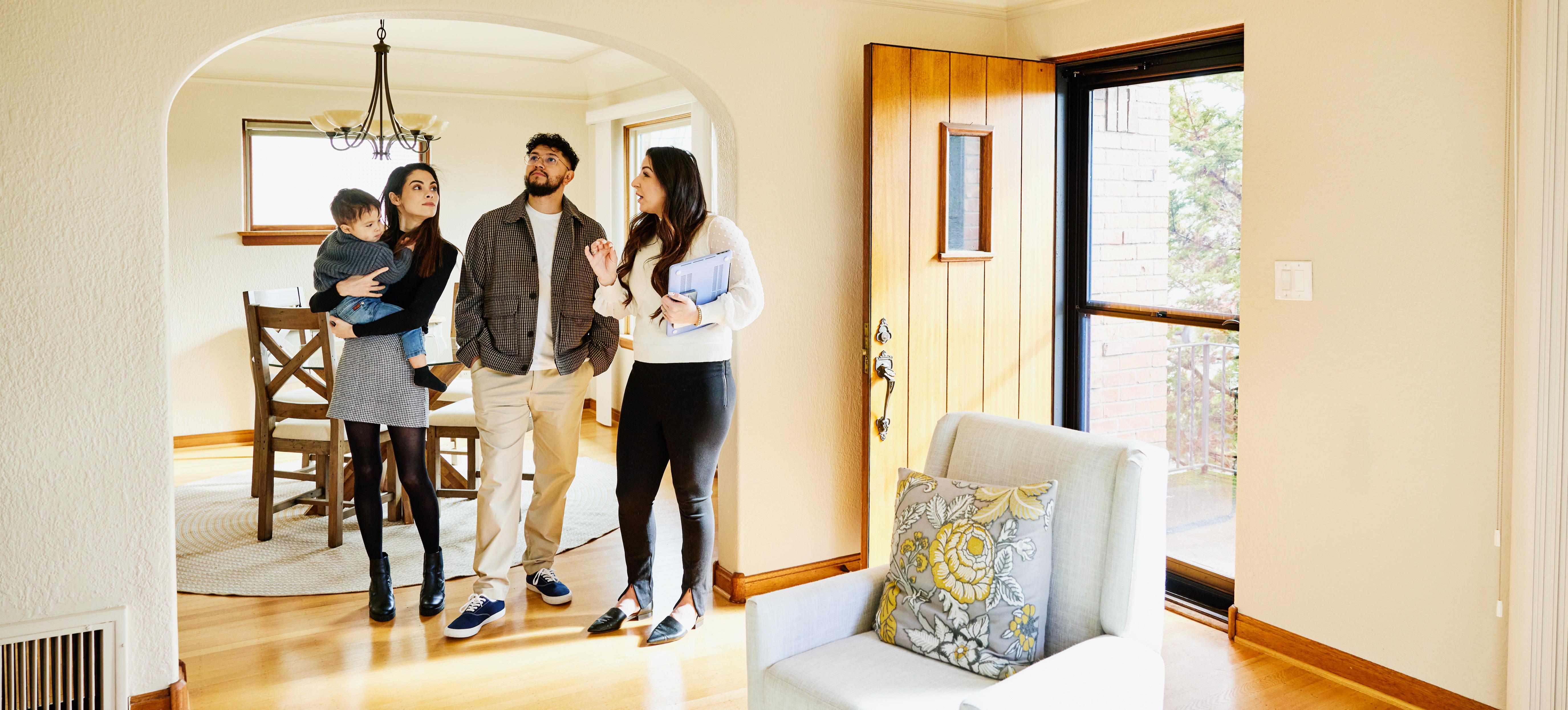 [Featured Image] A real estate agent practices her real estate agent skills as she gives a house tour to a young family who are potential buyers.
