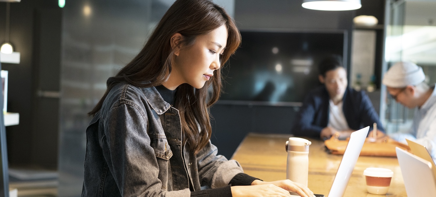 [Featured image] A young person sits at a communal office table and uses their laptop to research transfer degrees.