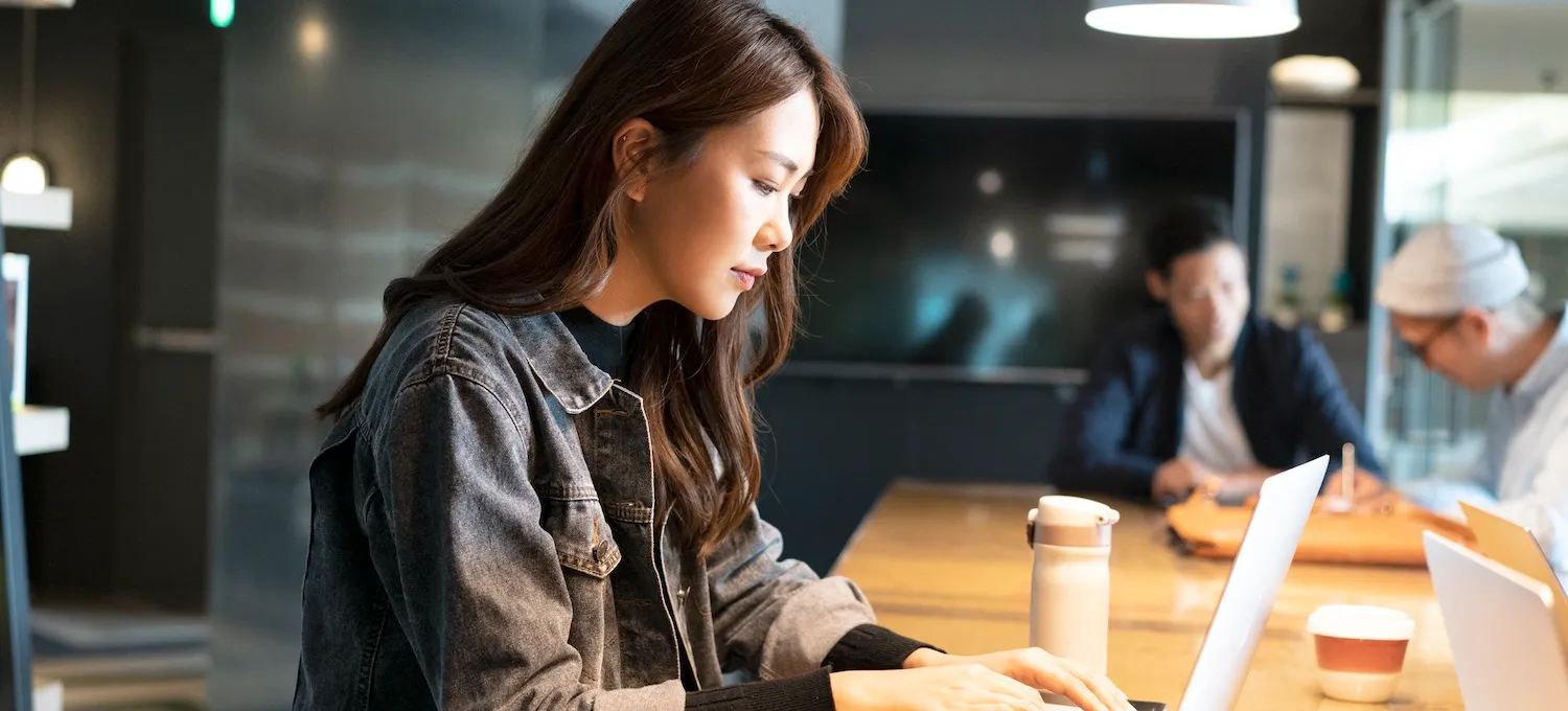 [Featured image] A young person sits at a communal office table and uses their laptop to research transfer degrees.