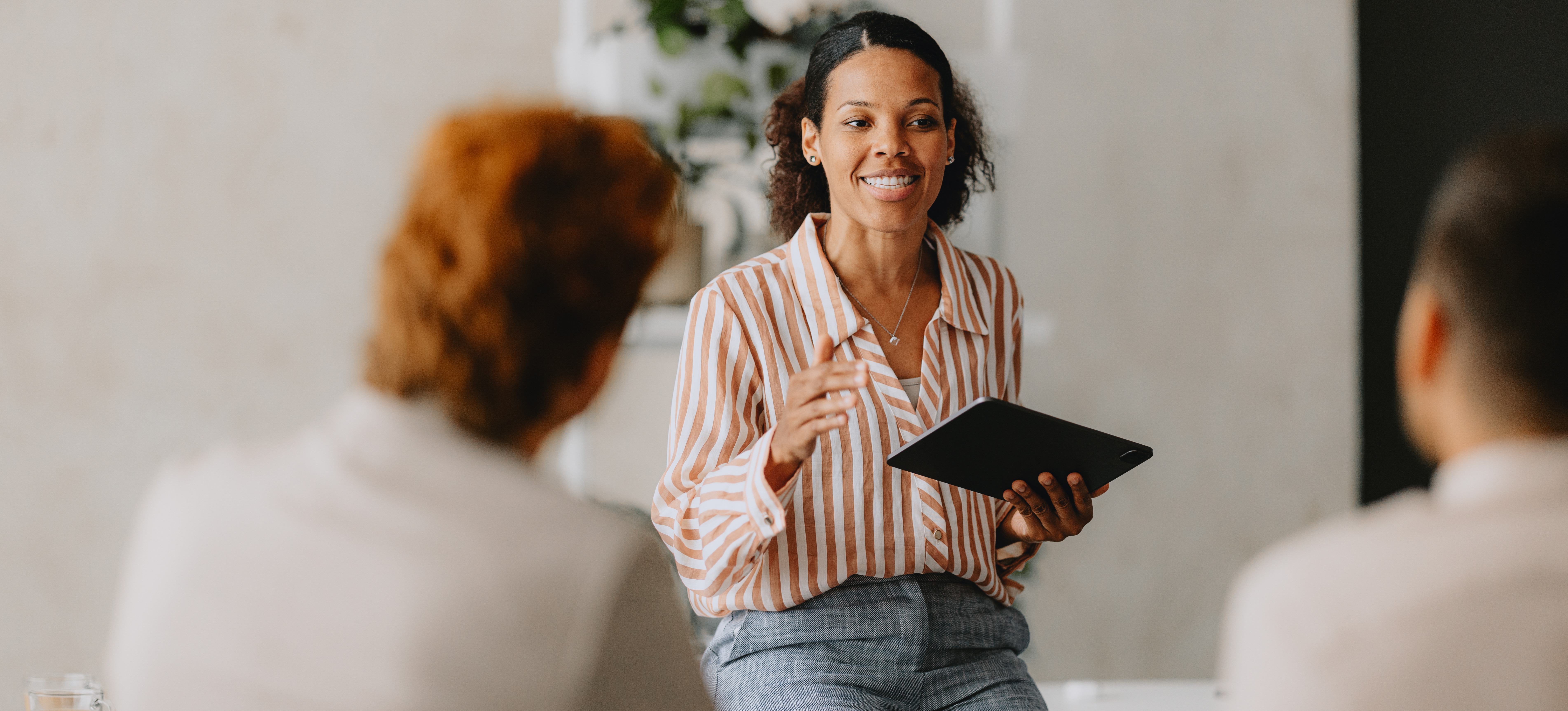 [Featured Image]: A woman holding a tablet speaks to members of the human resources department to discuss how the department's successes and set goals.
