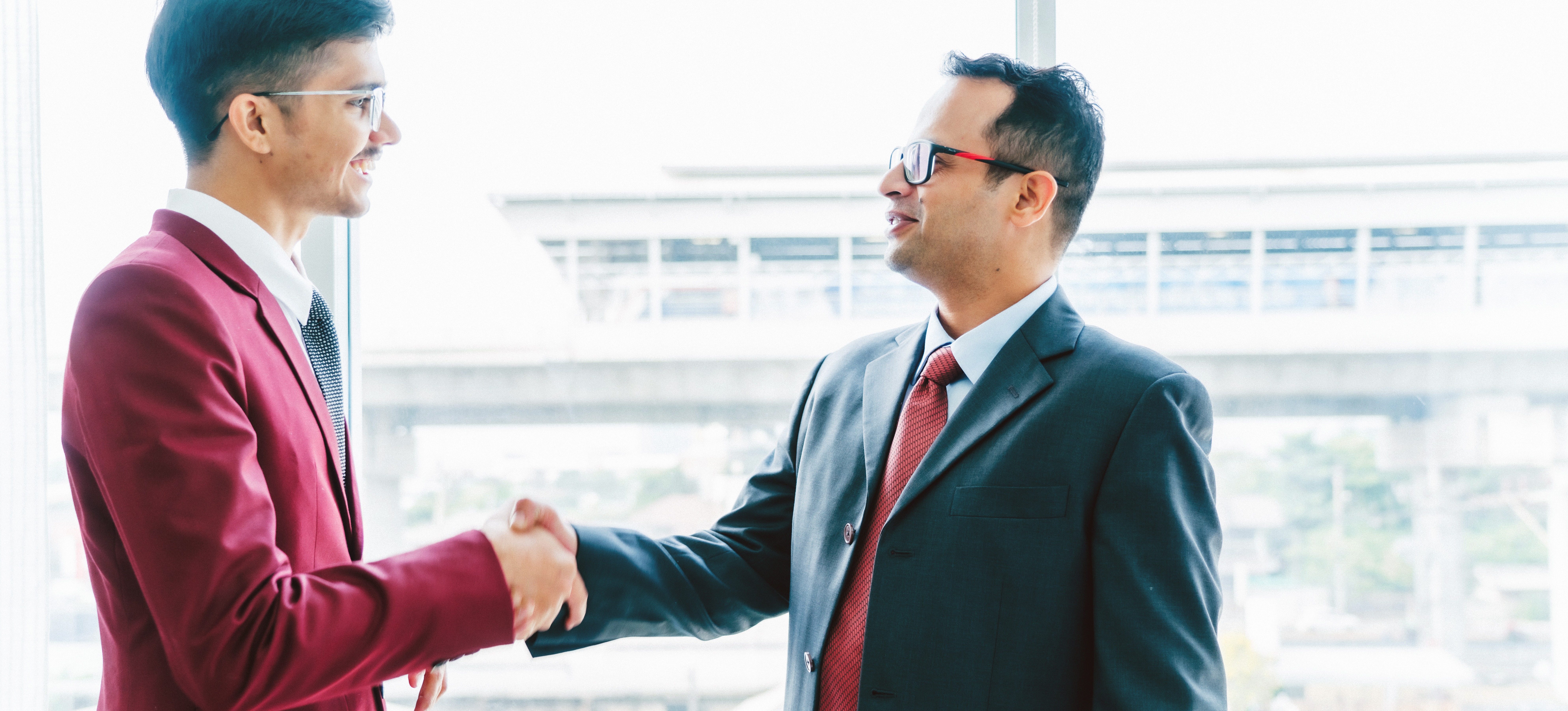 [Featured Image] A young man wearing a suit shakes hands with a potential employer after a job interview for one of the many jobs for freshers. 
