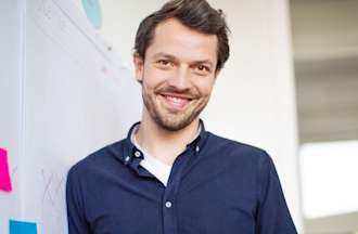 [Featured image] A project manager in a blue button-down leans against a whiteboard with colorful post-it notes on it.