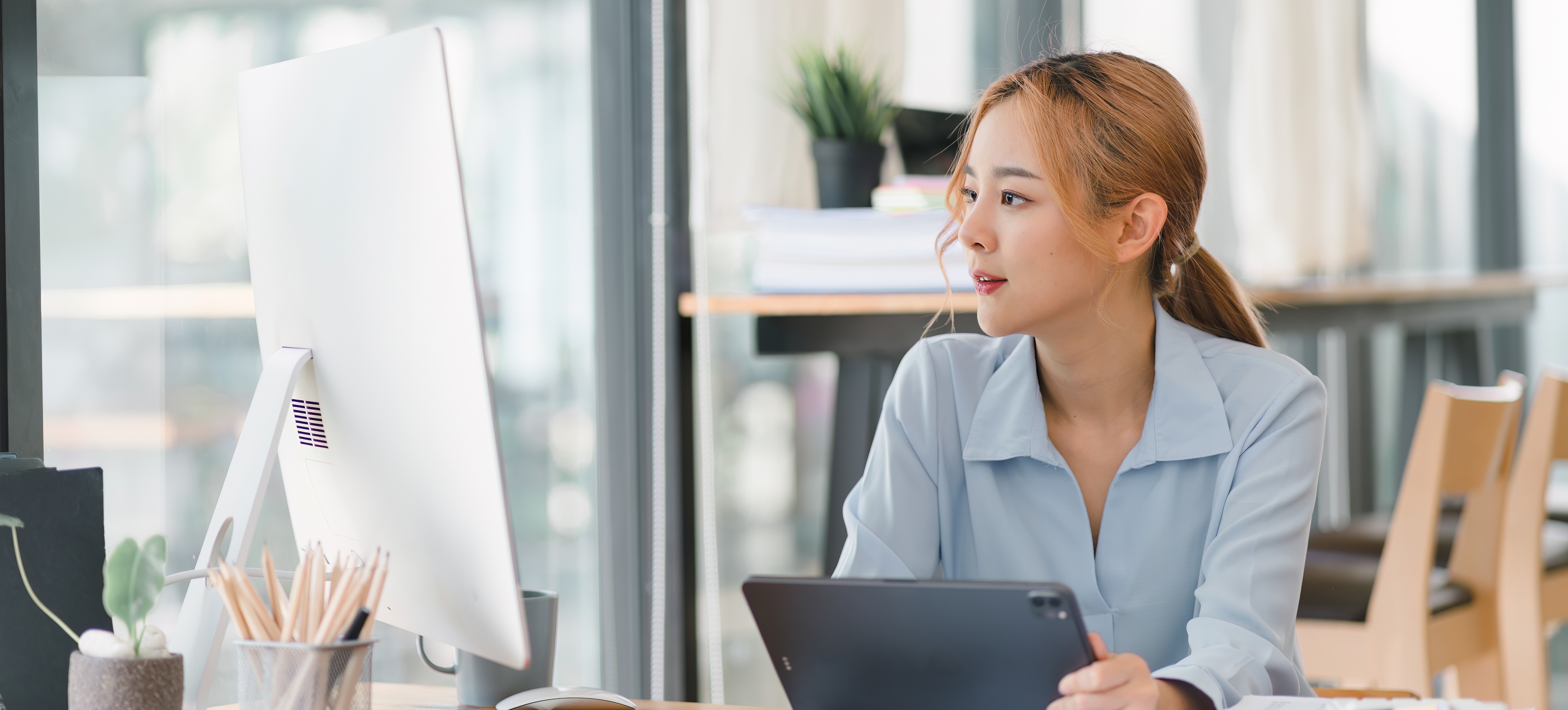 [Featured Image] A sales analyst compares data on their computer and tablet as they sit at their desk in a sunny office.