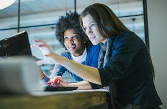 [Featured Image] Two people examine a laptop screen together in an office environment.