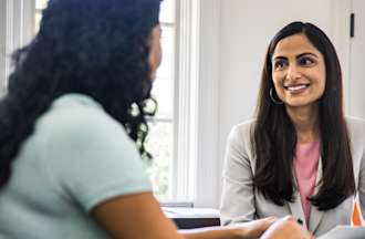 [Featured Image] A potential employer sits at a meeting table and smiles at a prospective employee holding their information technology resume.