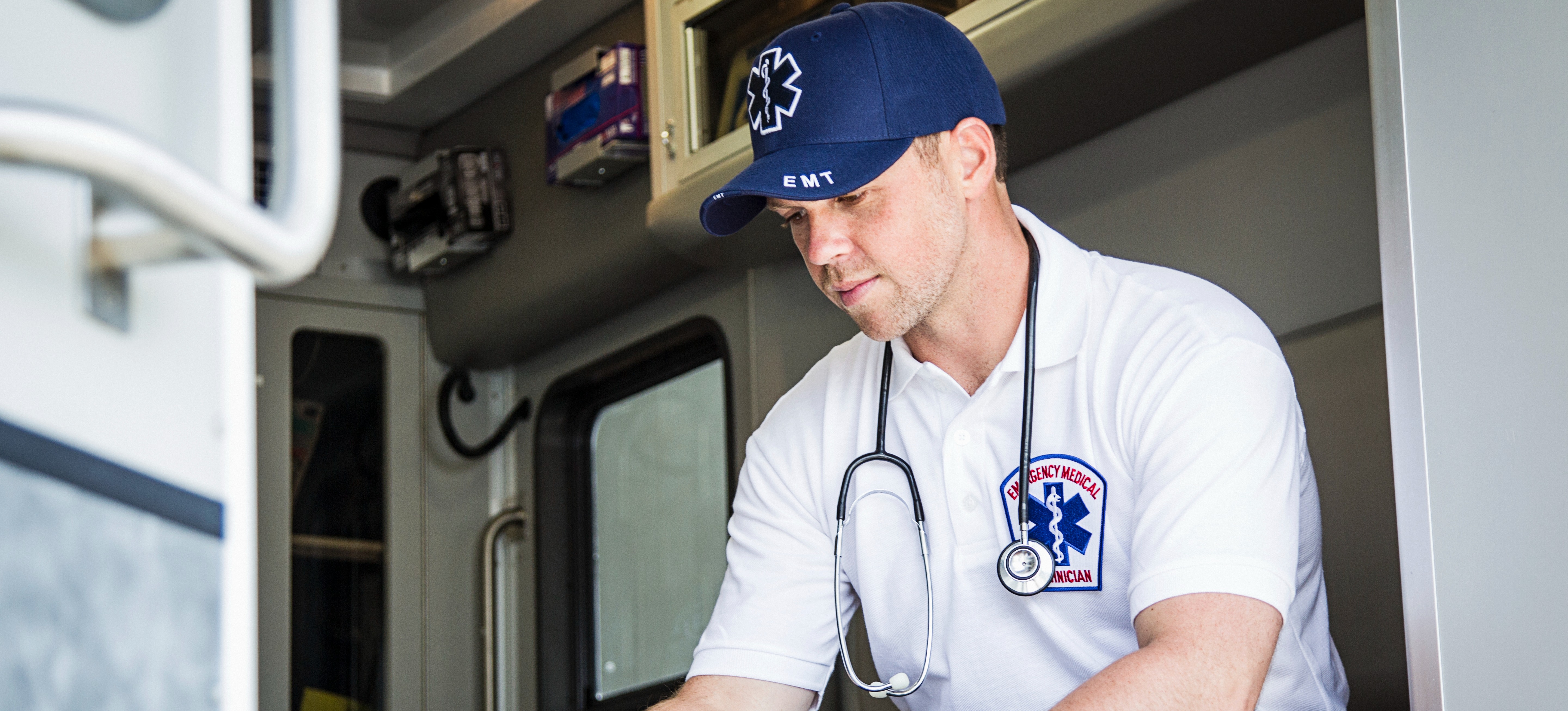 [Feature Image] An emergency medical technician reviews orders on a tablet while sitting in the back of an ambulance with a stethoscope around their neck.
