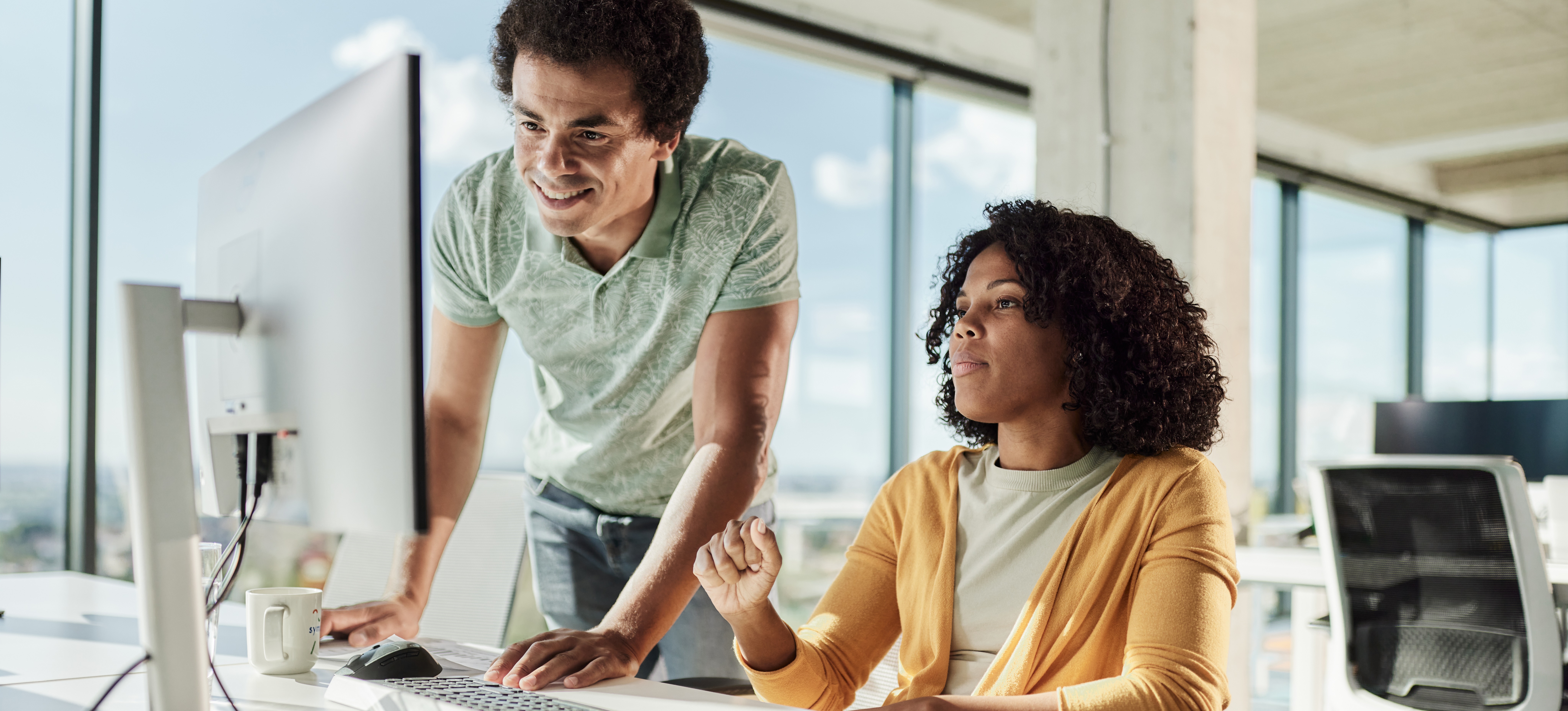 [Featured Image] Two artists in front of a computer, discussing how to describe a design to an AI art generator.

