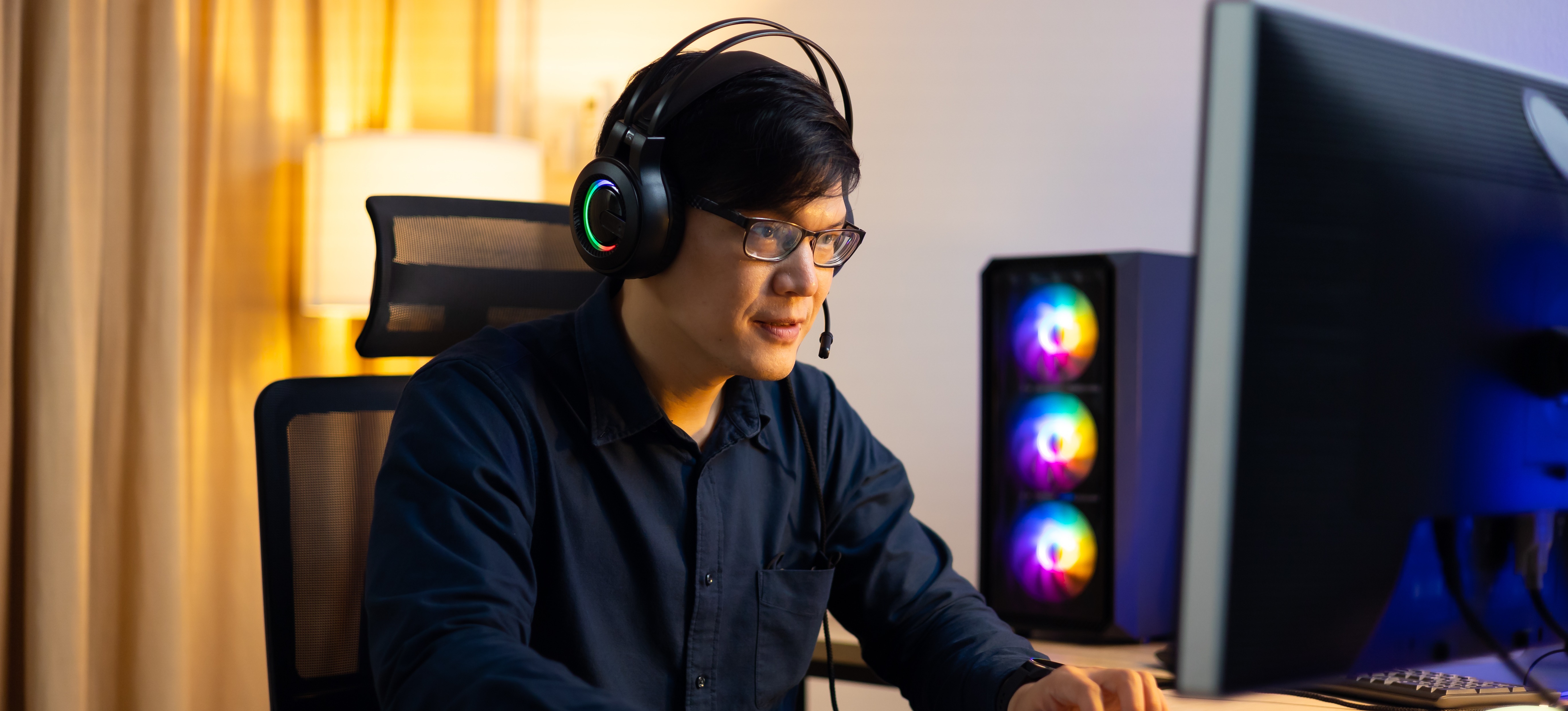 [Featured Image] A video game developer wears headphones and works at a computer, creating a video game.

