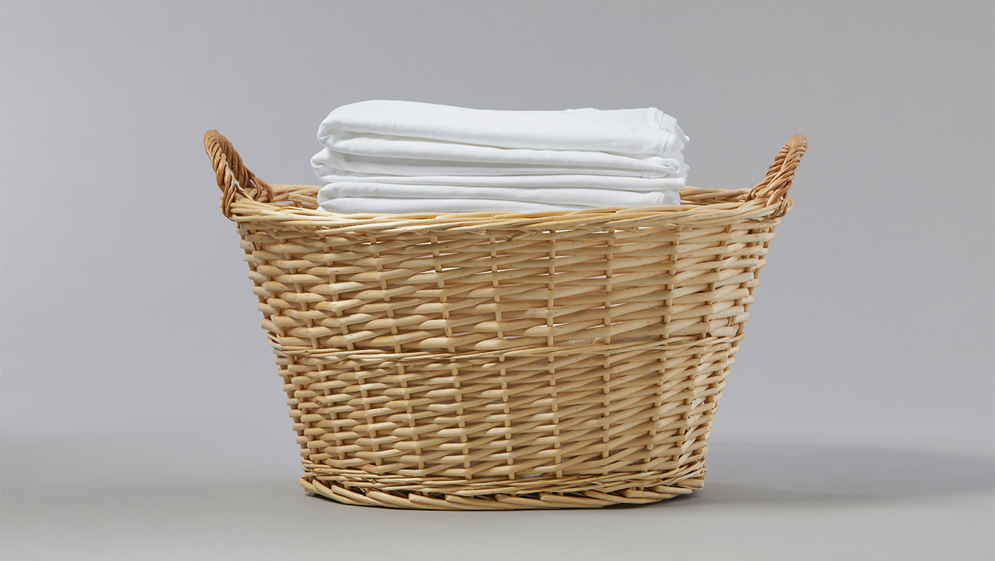 A woven laundry basket full of neatly folded, white garments