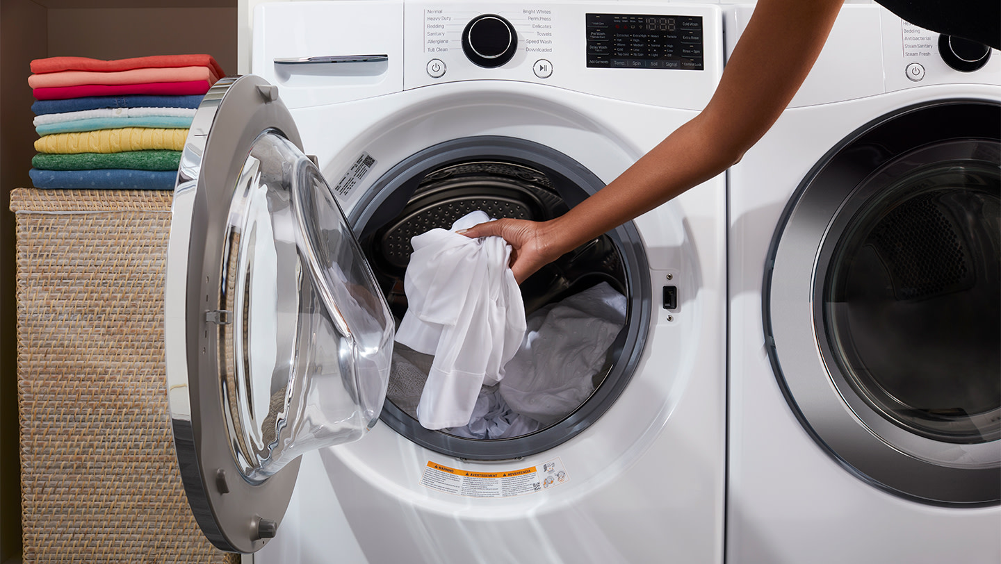 A person loading white clothes into the washing machine drum