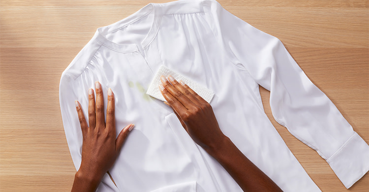 A person removing excess stain from a white shirt with a toothbrush with a paper towel