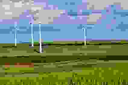 Four wind turbines in an open green field of grass.