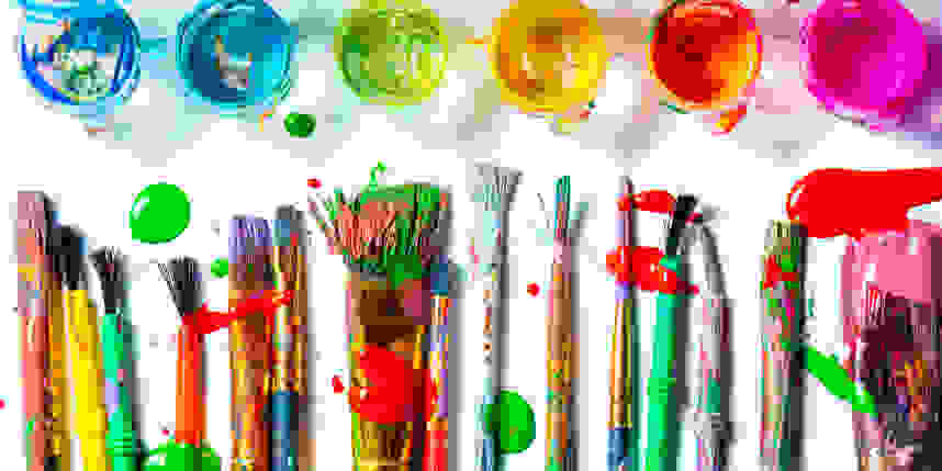 Paint brushes scattered on a table and surrounded by various colors of paint