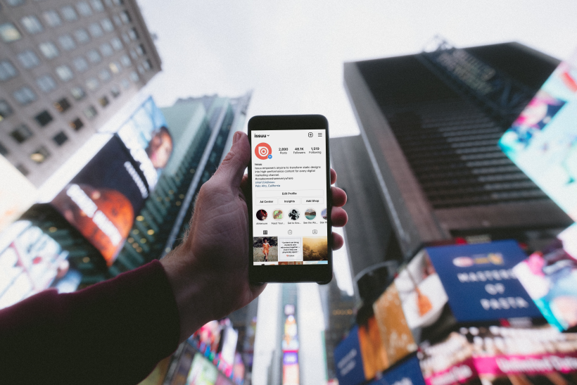 A hang holding up a phone with Issuu's Instagram page displayed on the screen. Behind the hand holding up the phone is city background with skyscrapers framing the photo